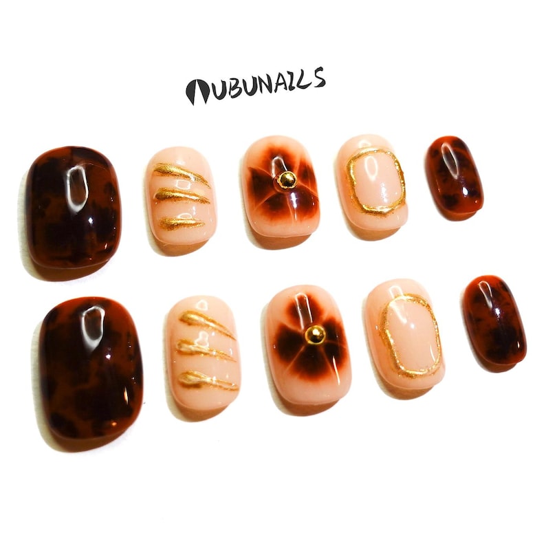 Short almond-shaped handmade press-on nails in ombre brown and peach gold tones. 3D gel design features free-style sculpted flowers, giving a delicate and elegant look. The nails have a clean, simple finish, perfect for daily wear or special occasions like birthday partiy. Subtle shimmer adds a festive touch, making them an ideal gift for her. Displayed neatly in a set, highlighting the smooth glossy texture and intricate floral details. Suitable for OOTD styling or gifting as a birthday present