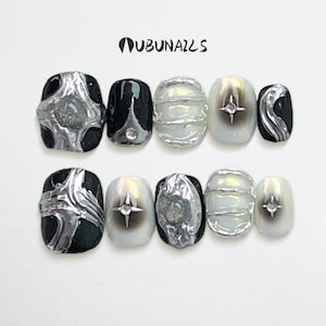 Op de afbeelding: Een set van tien kunstnagels met een futuristisch ontwerp. De nagels hebben een mix van zwart, zilver en iriserend wit. Sommige nagels hebben stervormige accenten, andere hebben getextureerde zilveren versieringen. De merknaam "UBUNAILS" staat bovenaan.