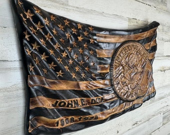 May include: A wooden American flag with a distressed finish. The flag is carved with the Great Seal of the United States and the text "JOHN E. DOE 1968-1970".