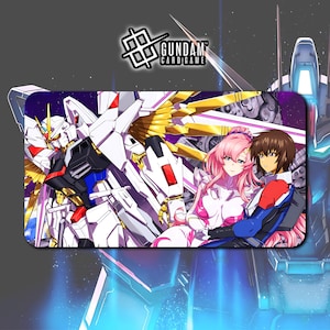 May include: A rectangular Gundam card game playmat featuring a white and gold mecha robot and two anime characters. The playmat has a dark purple background with the Gundam Card Game logo in the top left corner.