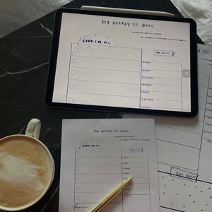 Könnte beinhalten: Ein weißer Wochenplaner mit einem schwarzen Stift und einer Tasse Kaffee. Der Planer hat einen Bereich für "Work on it's" und einen Bereich für Termine. Der Planer hat auch einen Habit Tracker mit einem Kalender.