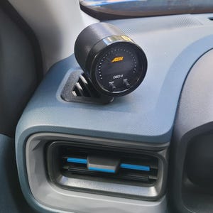 Può includere: Un manometro OBD-II AEM nero montato su un cruscotto blu. Il manometro ha un display digitale e due pulsanti con l'etichetta "PAGE" e "ESC". Il manometro è posizionato sopra una presa d'aria dell'auto.