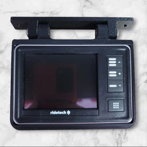 May include: A black Ridetech GPS device with a screen, buttons, and a grid-like button. The device is mounted on a black bracket.