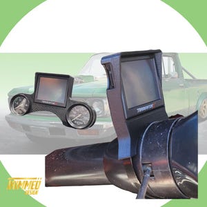 Puede incluir: Un soporte de tablero negro con una pantalla que muestra el texto "Terminator X". El soporte está unido a un volante negro. El fondo muestra una camioneta verde con un tablero personalizado.