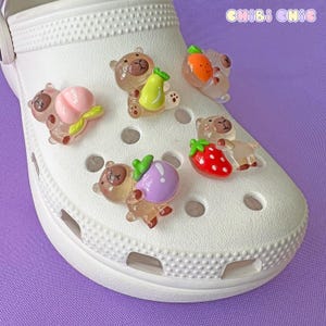 May include: White clog shoe with six brown bear charms with fruit accents. The charms include a peach, pear, strawberry, purple plum, and two orange slices.