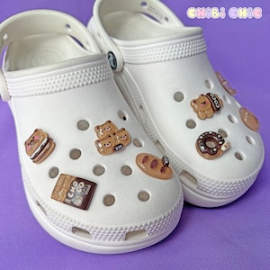 May include: White clogs with various brown and white charms attached. The charms include a bear, a donut, a chocolate bar, and a loaf of bread. The text "Chibi Chic" is visible on the top of the image.