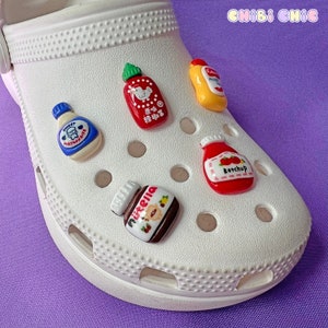 May include: White clog shoe with various miniature condiment bottles attached to it. The bottles include ketchup, mayonnaise, mustard, Nutella, and a bottle with Japanese text.