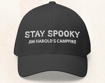 Puede incluir: Gorra de béisbol negra con la frase bordada "STAY SPOOKY" sobre "JIM HAROLD'S CAMPFIRE" en blanco. La gorra tiene una visera curva y un ajuste estructurado.