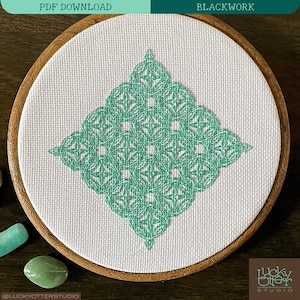 May include: A teal green geometric pattern is embroidered on white fabric in a round wooden embroidery hoop. The hoop is on a brown wooden surface with three teal green stones.