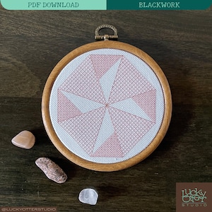 May include: A pink and white geometric cross-stitch design in a wooden embroidery hoop. The design is a repeating pattern of triangles and squares.