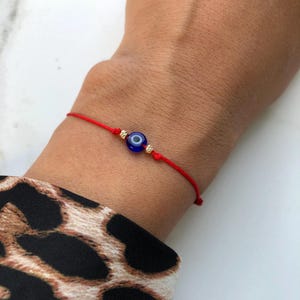 Könnte beinhalten: Rotes Armband mit einem blauen Glücksbringer-Auge und goldenen Perlen.
