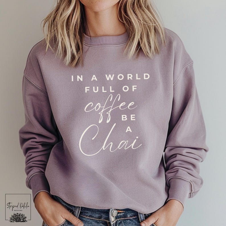 Puede incluir: Una sudadera de color morado con el texto "In a world full of coffee be a chai" impreso en la parte delantera.