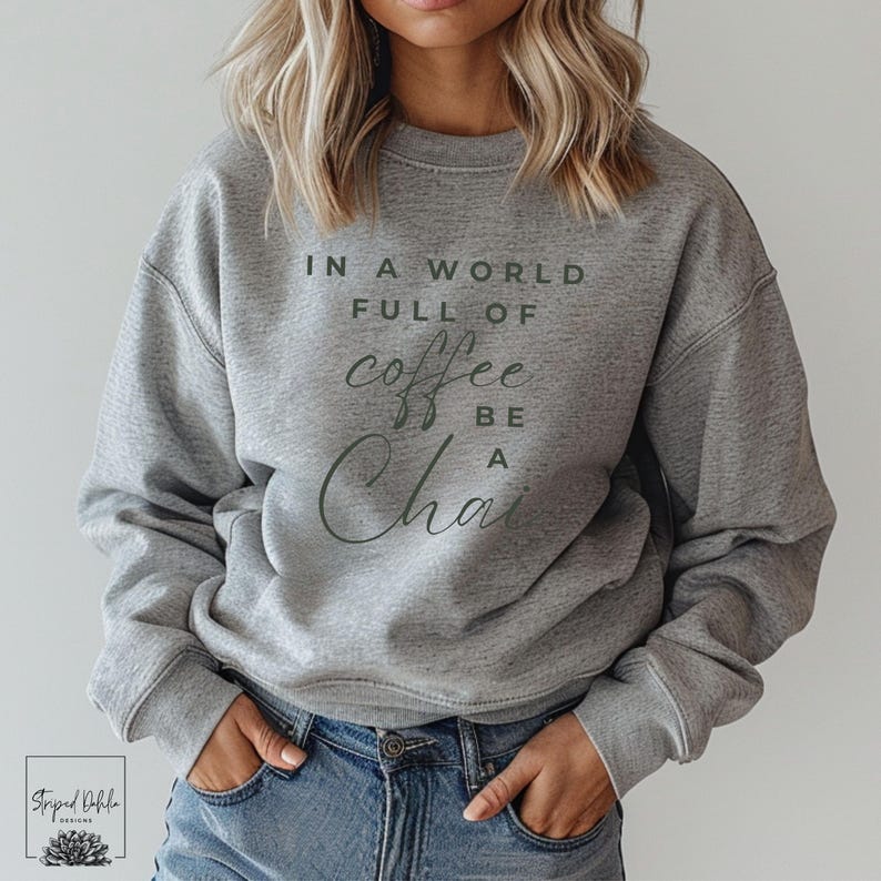 Puede incluir: Sudadera gris con el texto "In a world full of coffee be a chai" impreso en la parte delantera.