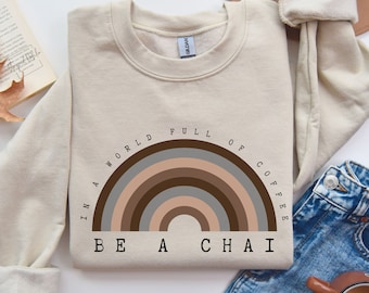 Może przedstawiać: Beżowa bluza z grafiką tęczy i tekstem "In a world full of coffee be a chai".