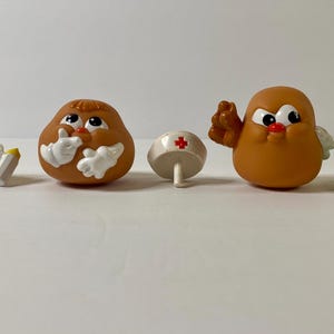 May include: A set of Mr. Potato Head pieces, including a brown potato head with a white nurse's hat, a brown potato head with a yellow and white baby bonnet, a green hat, a white bottle, and a yellow and white baby bonnet.