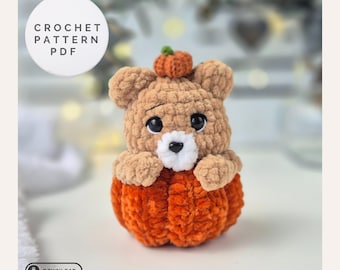 May include: A crocheted bear sits inside an orange pumpkin. The bear is light brown with a small pumpkin on its head. The image includes the text "CROCHET PATTERN PDF" and a download button.