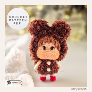 May include: A handmade crochet doll with a brown furry hood and matching outfit. The doll has a light brown face, large black eyes, and red shoes. The image includes text that says "CROCHET PATTERN PDF" and "DOWNLOAD".