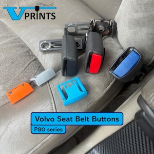 以下が含まれることがあります： 黒、赤、青、オレンジ、グレーなど、さまざまな色のボルボシートベルトボタンのコレクション。画像には「Volvo Seat Belt Buttons」と「P80 series」の文字が含まれています。ボタンは車のシートに表示されています。