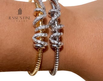 Könnte beinhalten: Zwei schlangenförmige Armbänder, eines in Gold- und eines in Silberoptik, mit gewundenen Körpern und klaren Steinakzenten auf der Oberseite. Der Text JESSE'S FINE JEWELRY ist neben dem goldenen Armband sichtbar. Die Armbänder haben ein strukturiertes Band.