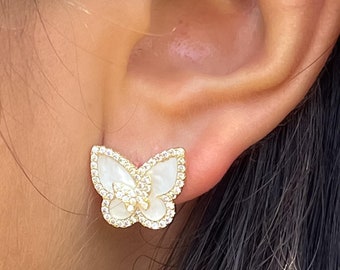 Puede incluir: Un par de pendientes de mariposa de oro con alas de nácar blanco y detalles de circonita cúbica transparente.