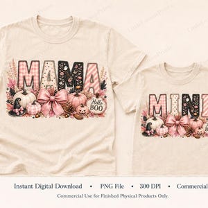 Könnte beinhalten: Zwei beige T-Shirts mit Grafikdrucken. Das größere T-Shirt zeigt den Schriftzug MAMA und das kleinere T-Shirt MINI. Beide Designs enthalten rosa Kürbisse, eine große rosa Schleife, einen Hexenhut und einen kleinen Kürbis mit der Aufschrift Hello BOO.
