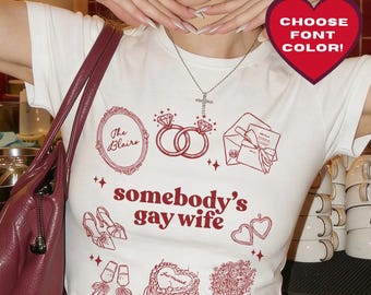 May include: White t-shirt with red graphic illustrations and the text "somebody's gay wife." The shirt features wedding-themed designs and the text "Choose Font Color!" on a heart-shaped sticker. A burgundy purse is visible.