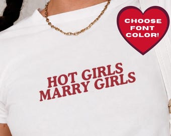 May include: A white short-sleeved t-shirt featuring the red text HOT GIRLS MARRY GIRLS printed on the chest. The shirt is paired with a gold chain necklace and a white shoulder bag with gold hardware. A heart-shaped graphic says CHOOSE FONT COLOR.