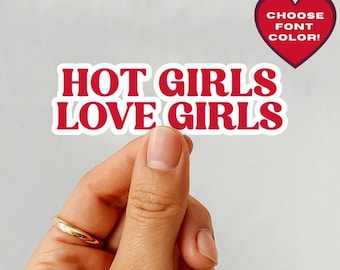 Op de afbeelding: Een sticker met de tekst "HOT GIRLS LOVE GIRLS" in het rood, omlijnd met wit. Een rood hart met de tekst "CHOOSE FONT COLOR!" is ook zichtbaar. De sticker wordt vastgehouden door een hand met een gouden ring.