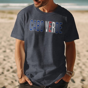 Puede incluir: Camiseta azul marino con el texto "CABO VERDE" en un diseño azul, blanco y rojo. La camiseta está hecha de un material suave y se lleva en una playa.
