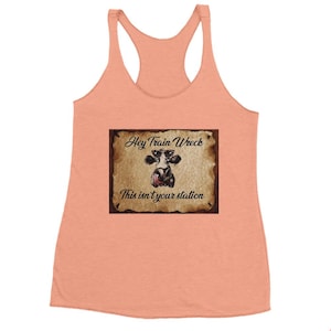 Puede incluir: Un top de tirantes color melocotón con un cartel marrón desgastado que presenta una vaca de dibujos animados con gafas de sol y el texto "Hey Train Wreck This isn't your station".