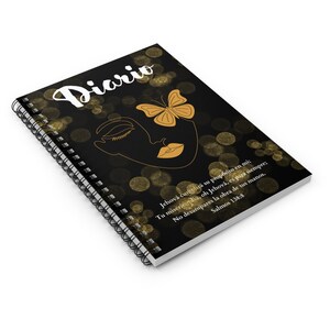 Puede incluir: Diario de espiral negro con un diseño de mariposa dorada y rostro de mujer. La portada presenta el texto "Diario" y una cita en español: "Jehová cumplirá su propósito en mi; Tu misericordia, oh Jehová, es para siempre; No desampares la obra de tus manos. Salmos 138:8"