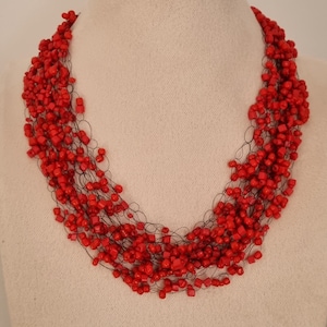 May include: A red beaded necklace with multiple strands of small, square-shaped beads. The necklace is made with a thin, black wire that connects the beads.