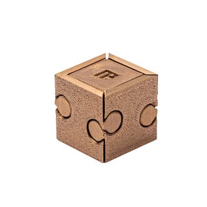 Peut inclure: Un cube puzzle de couleur bronze avec une surface texturée. Le cube comporte des pièces imbriquées et un motif sur une face. Le puzzle est conçu pour être résolu en manipulant les pièces pour qu'elles s'emboîtent.