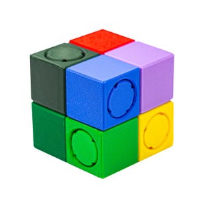 Puede incluir: Un rompecabezas de cubo colorido con seis lados, cada uno de un color diferente: rojo, morado, amarillo, verde, azul y verde oscuro. Cada cara tiene una hendidura circular. Un juguete vibrante.