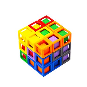 Op de afbeelding: Een kleurrijke kubuspuzzel met heldere kleuren, waaronder rood, geel, groen, oranje, blauw, paars en grijs. De kubus is gemaakt van in elkaar grijpende vierkante frames en kleinere gekleurde vierkanten.