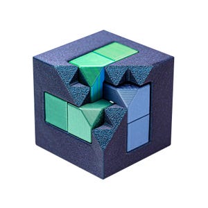 Könnte beinhalten: Ein geometrischer Puzzle-Würfel mit dunkelblau strukturierter Außenseite und verschiedenen farbigen Innenteilen. Das Puzzle hat grüne und blaue Komponenten, die ein visuell ansprechendes Design schaffen. Die Kanten des Würfels haben ein strukturiertes, eckiges Design.