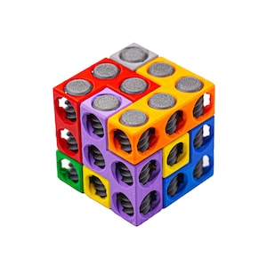 Könnte beinhalten: Ein farbenfrohes Würfelpuzzle mit ineinandergreifenden Blöcken in Rot, Orange, Gelb, Grün, Blau und Lila. Jeder Block hat eine graue, strukturierte kreisförmige Oberseite und ein Spiraldesign. Ein lebendiges Lernspielzeug.