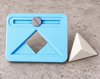 Può includere: Una cornice rettangolare in plastica azzurra dotata di un binario di scorrimento orizzontale con un piccolo bottone metallico circolare e un'ampia apertura triangolare al centro, accompagnata da un oggetto piramidale bianco solido.