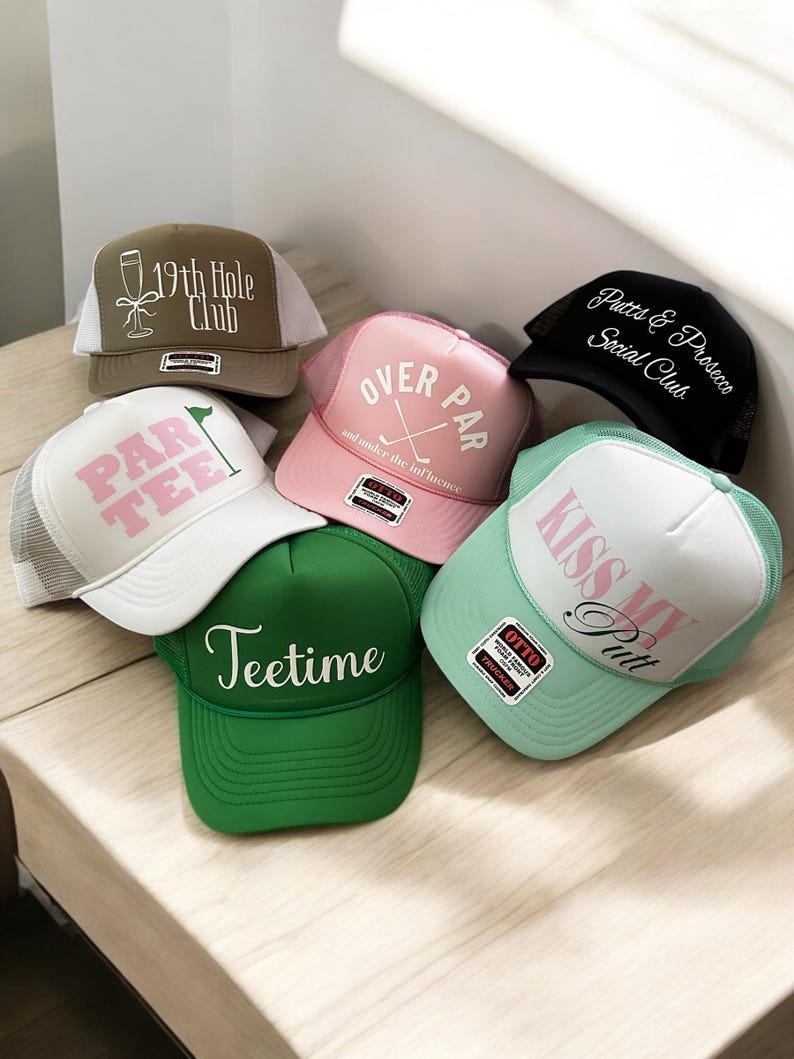 May include: Six different trucker hats with various golf-themed designs. The hats are in different colors, including green, pink, white, black, and brown. The designs include "19th Hole Club", "Par Tee", "Over Par", "Putts & Prosecco Social Club", "Kiss My Putt", and "Teetime".