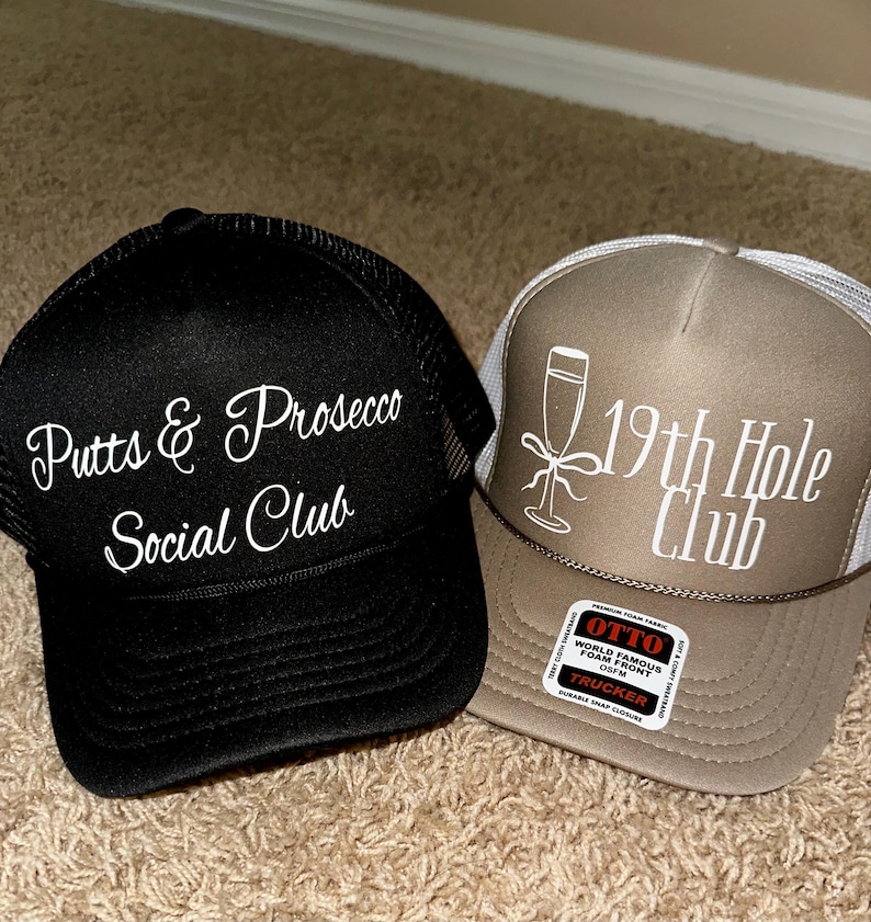 May include: Two black and brown trucker hats with white embroidered text. The black hat says "Putts & Prosecco Social Club". The brown hat says "19th Hole Club" and has a white glass of champagne graphic.