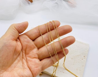 May include: A set of four gold chain necklaces, layered and displayed in a hand. The chains are thin and delicate, with a smooth, polished finish.