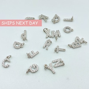 May include: A collection of silver letter charms with clear crystal embellishments. The letters include C, D, E, G, I, K, L, M, P, R, T, X, Y, and Z.  The charms are perfect for adding a personalized touch to jewelry.