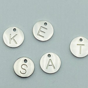 May include: Five silver metal round charms with letters K, E, S, A, and T engraved on them.