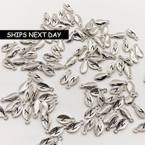 May include: A large quantity of silver-toned metal charms shaped like leaves with the letter "N" engraved on them. The charms have a small loop at the top for attaching to jewelry or other crafts.