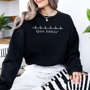 a woman sitting on a couch wearing a black sweatshirt