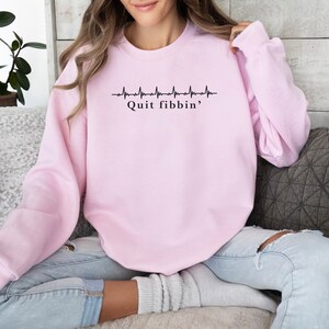 a woman sitting on a couch wearing a pink sweatshirt