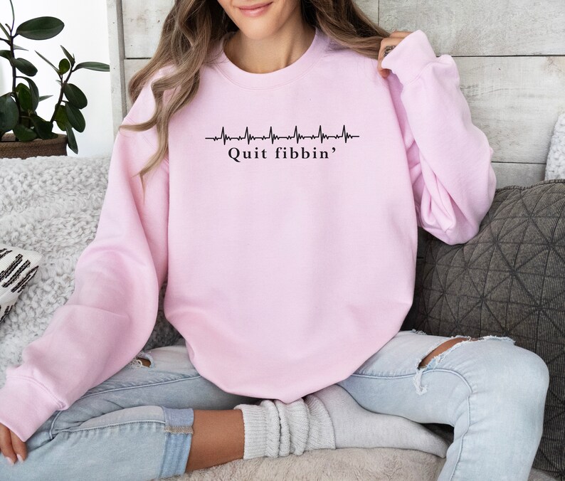 a woman sitting on a couch wearing a pink sweatshirt