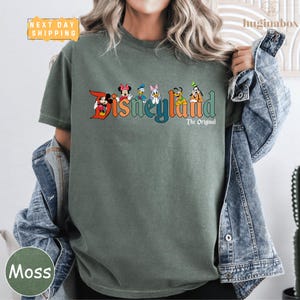 A person wearing a green t-shirt with the text "Disneyland The Original" printed on it, along with various Disney characters.