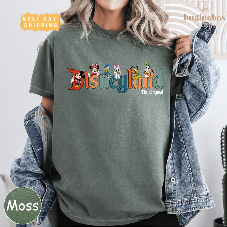 A person wearing a green t-shirt with the text "Disneyland The Original" printed on it, along with various Disney characters.