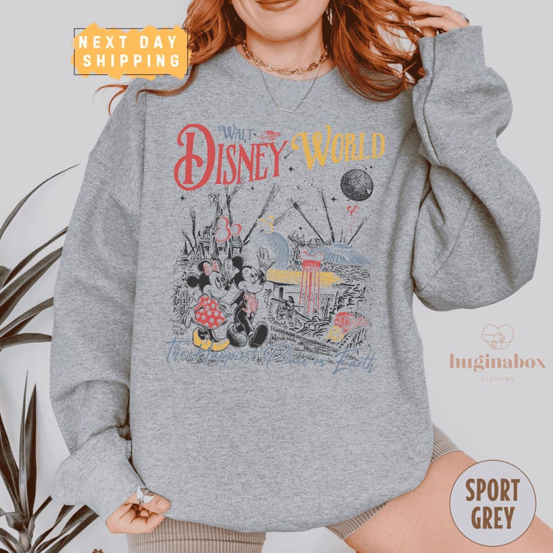 A person wearing a gray sweatshirt with a Disney World-themed graphic printed on it.
